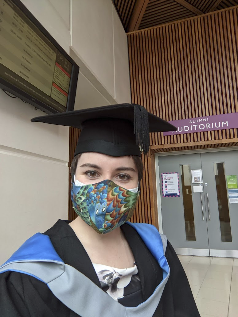 An image of the speaker in graduation attire, wearing two layers of mask.